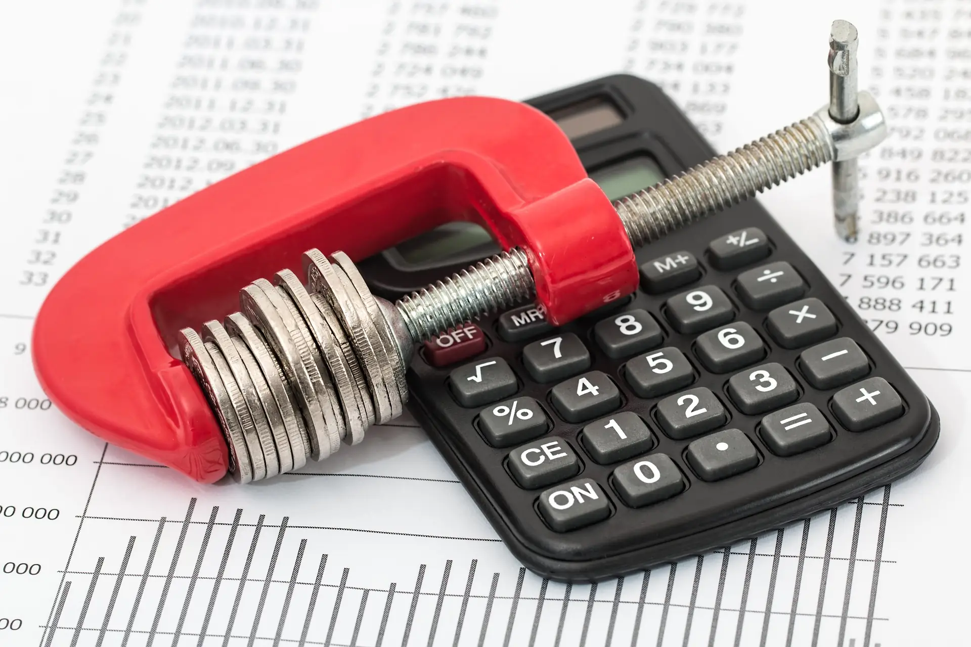 Stack of coins squeezed in a red clamp beside a calculator