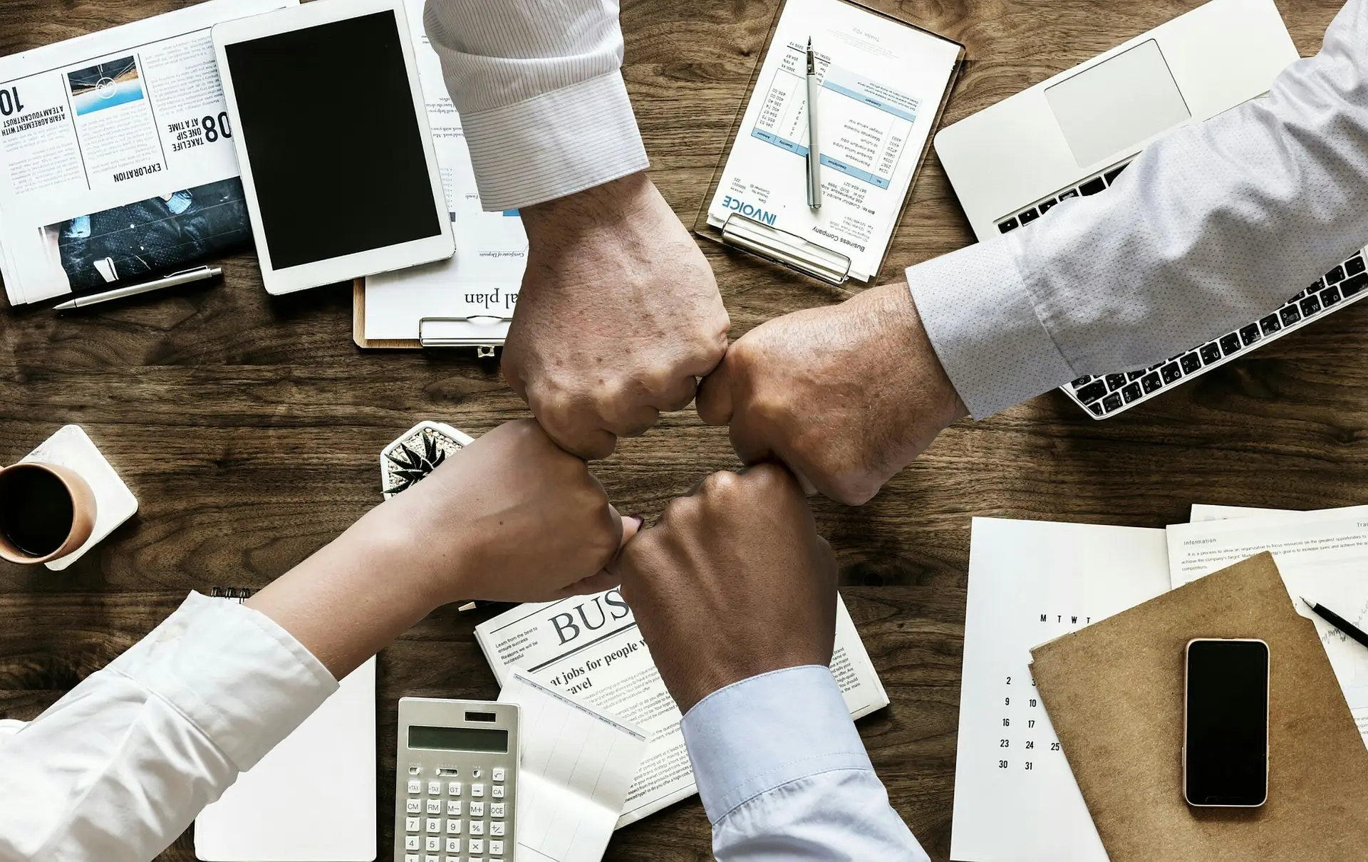 Colleagues bumping fists over a desk of papers, laptops and invoices
