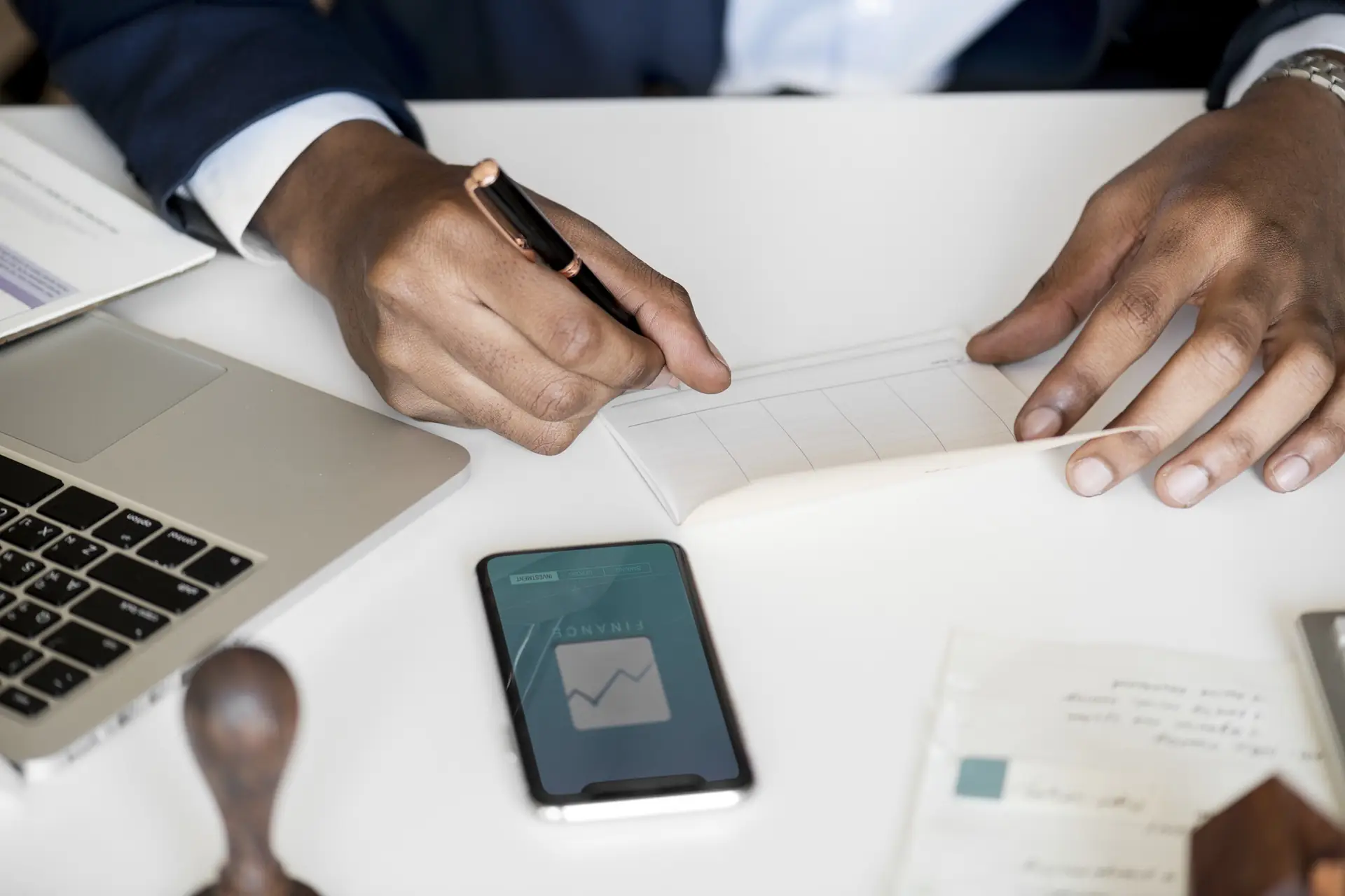 Hands signing a document beside a phone and a laptop